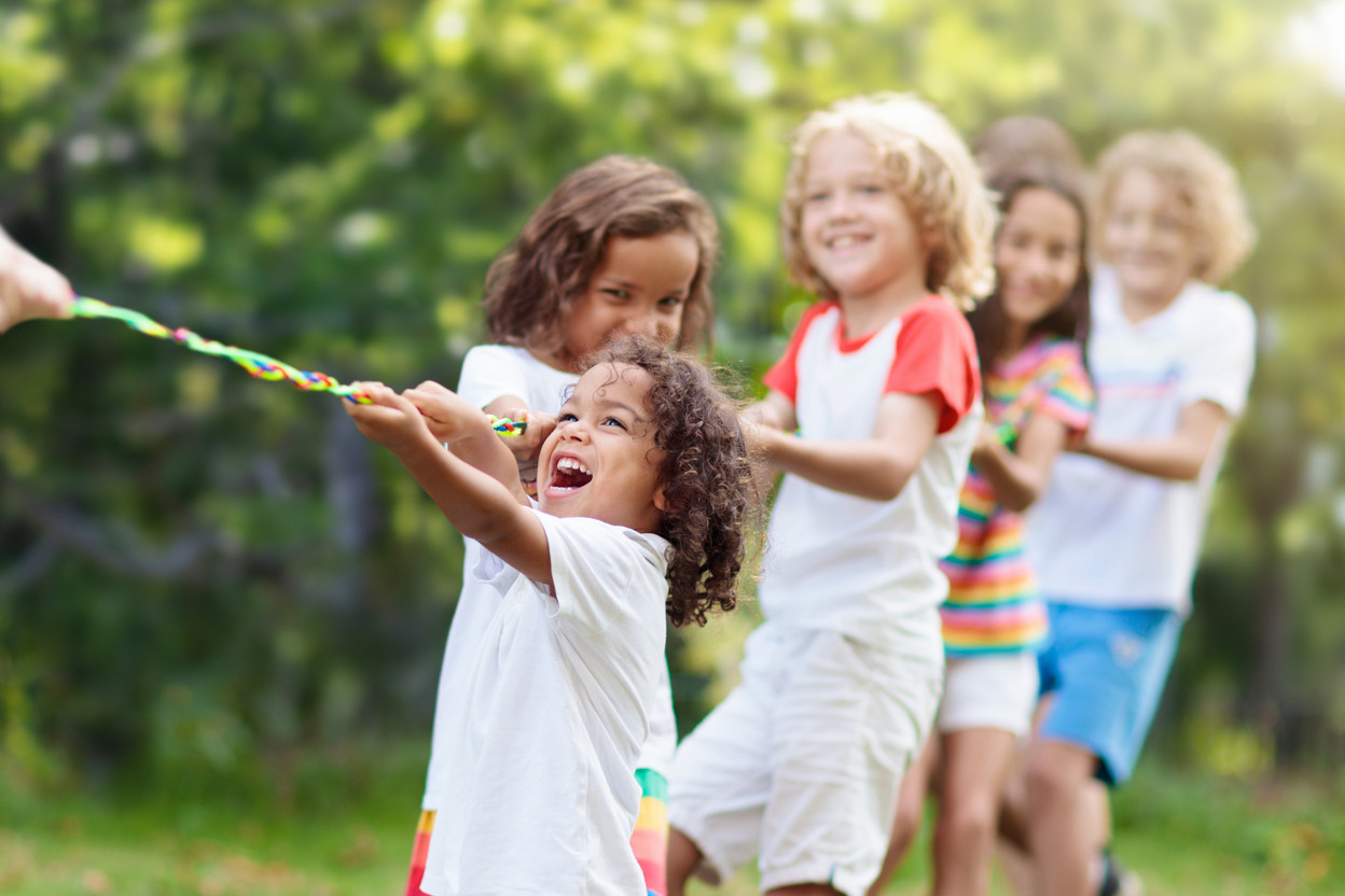 Kids play tug of war in sunny park. Summer outdoor fun activity. Group of mixed race children pull rope in school sports day. Healthy outdoor game for little boy and girl. (Photo: Copyright (c) 2022 FamVeld/Shutterstock.  No use without permission.)