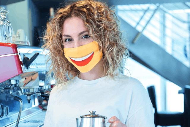 Photo shows one of the posters for the "Smile Again" campaign, featuring a barista wearing a mask with a smile on it Luxembourg Government