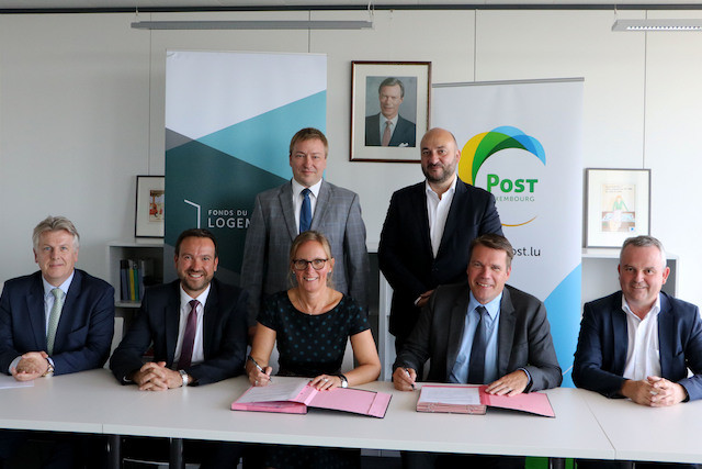 Pictured signing a €6m social housing property deal on 11 September 2018, from left: Jean-Paul Marc of the Housing Ministry, Luc Schockmel and Diane Dupont of the Housing Fund (Fonds du lodgement), Marc Hansen (the DP housing minister, standing), Étienne Schneider (the LSAP economy minister, standing), and Claude Strasser and Frank Reuter of Post Luxembourg MLOG