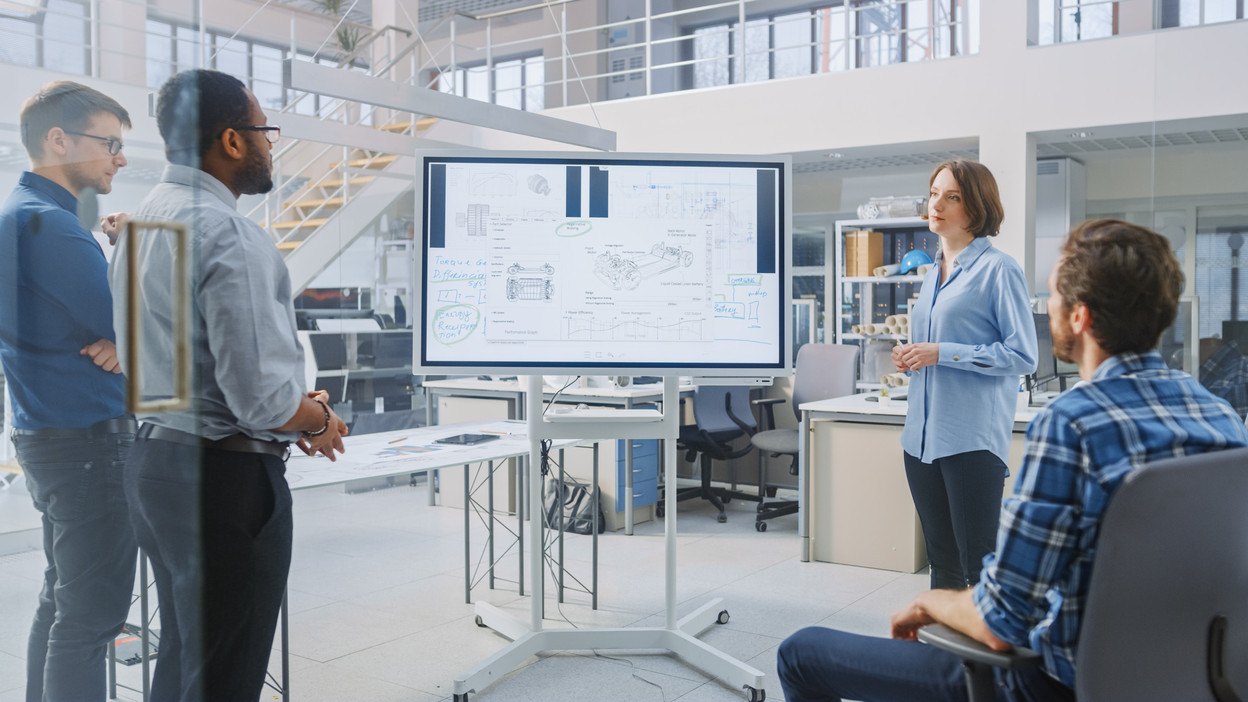 In the In Industrial Design Facility Team of Engineers and Technicians have a Meeting, Female Specialist Leads Briefing, Talks and Draws on Digital Interactive Whiteboard with Car Prototype Concepts Photo: Shutterstock.