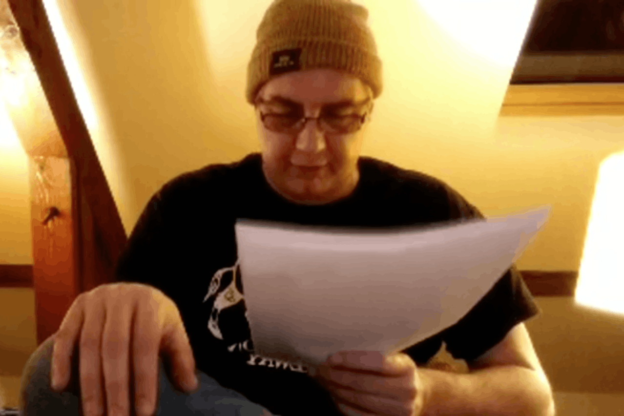 En ce mercredi 25 mars, l’auteur Francis Krips lit ses textes depuis chez lui, coiffé d’un bonnet et arborant un T-shirt avec un gros sanglier des Ardennes. (Photo: Capture d’écran/Facebook)