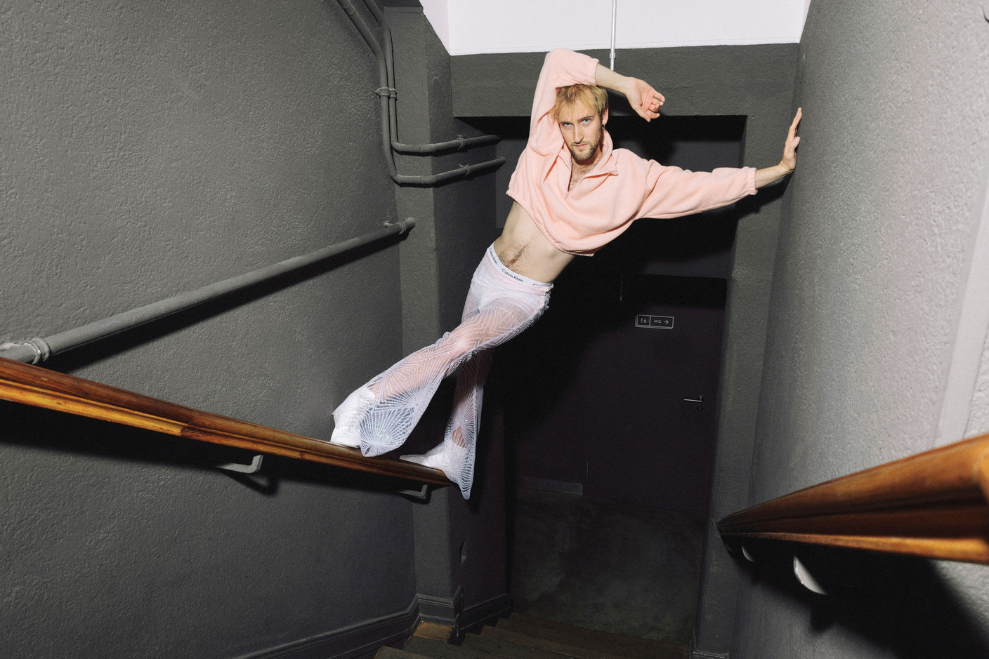 In a 24Colours sweater, Elsie Fred see-through pants and Calvin Klein briefs, he owns the staircase like an afterwork gone deliciously off-track. Photo: Julian Pierrot/Paperjam