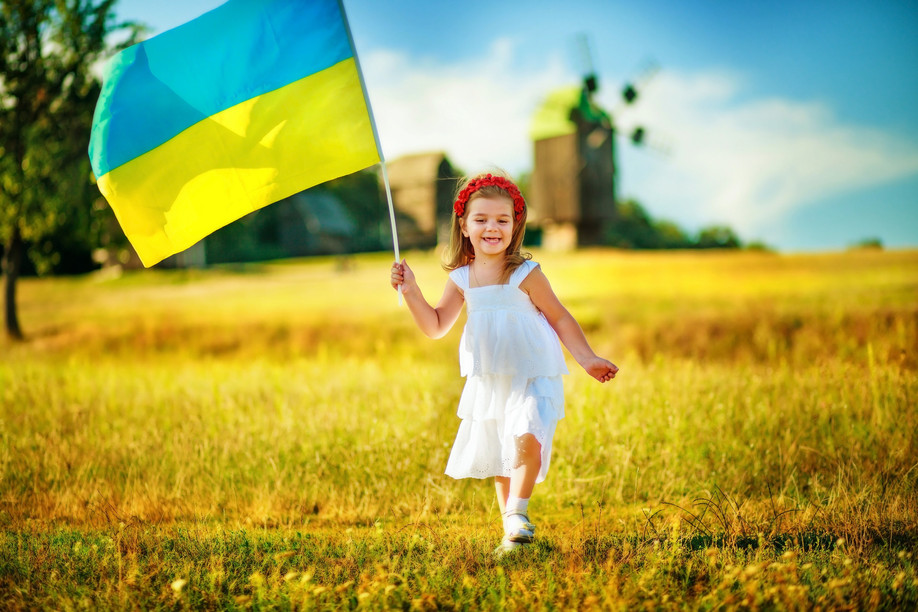 Child carries fluttering blue and yellow flag of Ukraine against background of mills in Pirogovo. (c) 2017 Lipatova Maryna/Shutterstock.