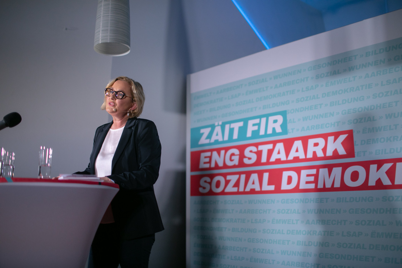 The deputy prime minister in front of a sign with the evocative slogan: “Zäit fir eng staark sozial Demokratie,” or “The time has come for a strong social democracy.”  Matic Zorman/Maison Moderne