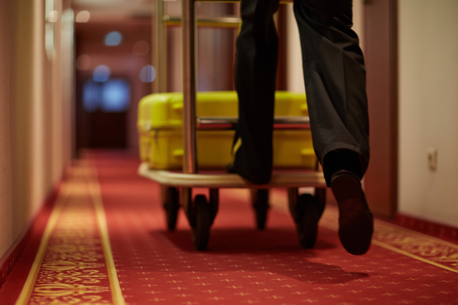 Porter moving luggage in cart down aisle covered by red carpet Pressmaster/Shutterstock.