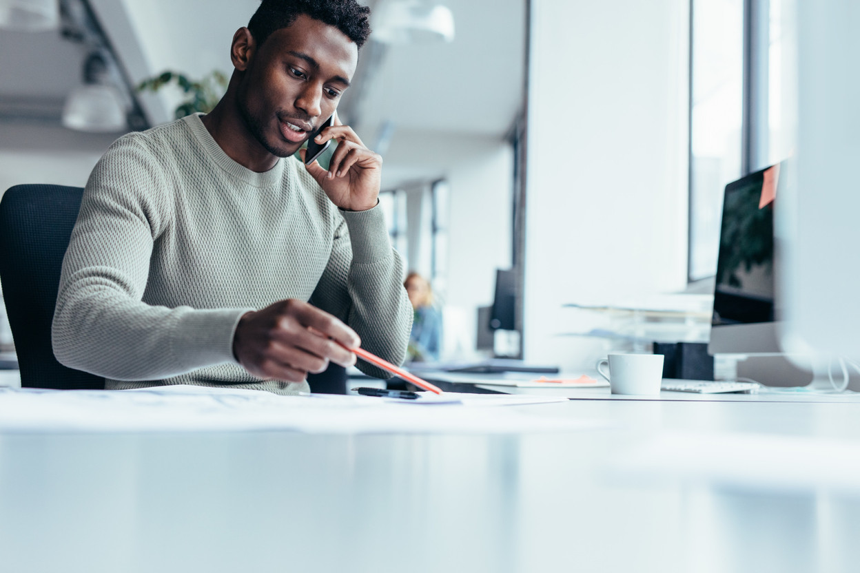 Businessman talking on smartphone and working in office. African male architect sitting at his workplace. Jacob Ammentorp Lund