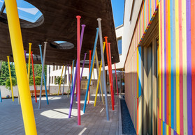 The entrance to the school is covered by a courtyard supported by a number of colourful posts. Photo: Christof Weber, Mathilde Magne