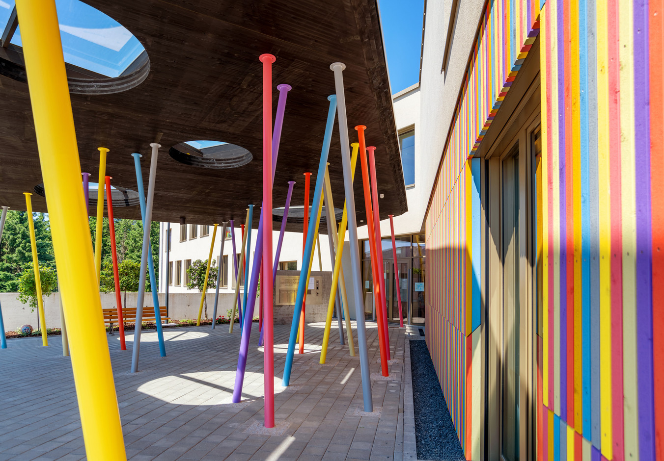The entrance to the school is covered by a courtyard supported by a number of colourful posts. Photo: Christof Weber, Mathilde Magne
